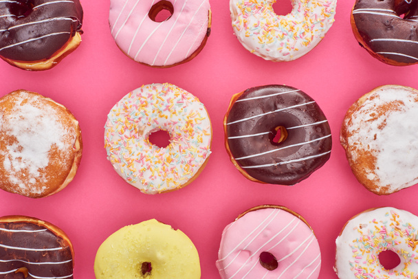 Top uitzicht van smakelijke geglazuurde kleurrijke donuts op Felroze achtergrond - Foto, afbeelding