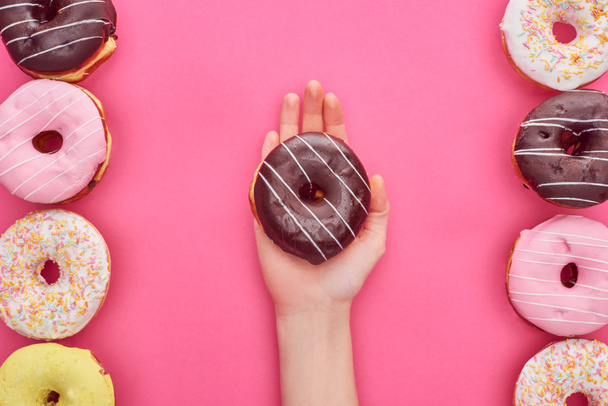partial view of woman holding chocolate doughnut on bright pink background - Φωτογραφία, εικόνα
