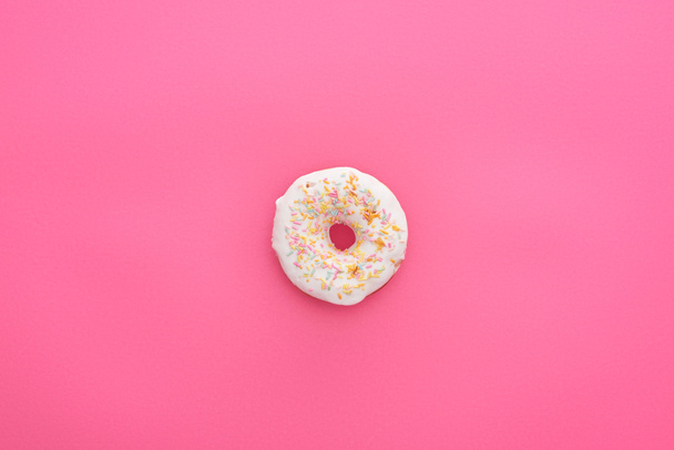 top view of tasty glazed white doughnut with sprinkles on bright pink background - Foto, imagen
