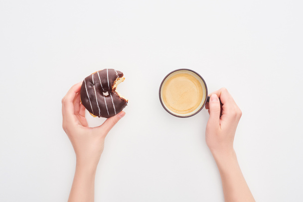 cropped view of woman holding tasty glazed bitten chocolate doughnut and coffee cup on white background - Фото, изображение