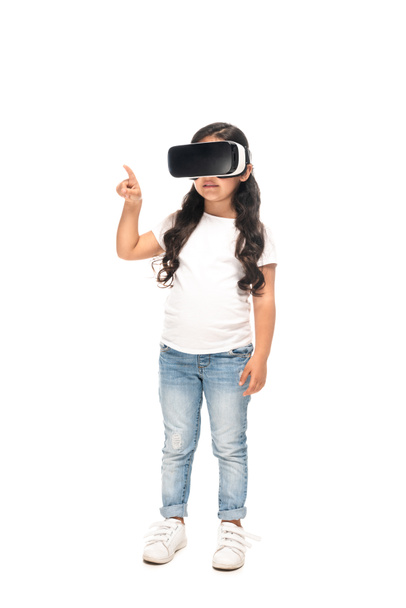 Λατινικό παιδί που σημαδεύει με δάχτυλο ενώ φοράει ακουστικά εικονικής πραγματικότητας απομονωμένα σε λευκό  - Φωτογραφία, εικόνα