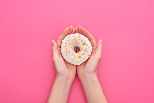 visão parcial da mulher segurando donuts de vidro branco com polvilhas no fundo rosa
 - Foto, Imagem
