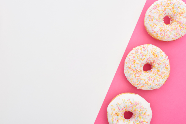 top view of glazed white doughnuts with sprinkles on white and pink background with copy space - Photo, Image