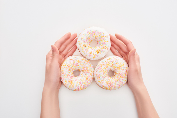 visão parcial da mulher segurando donuts brancos envidraçados com polvilhas no fundo branco
 - Foto, Imagem
