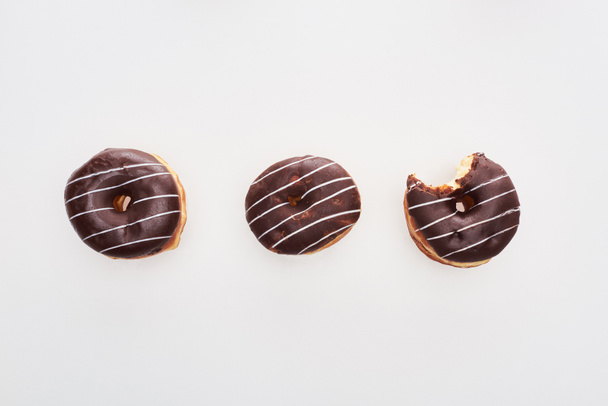 top view of chocolate tasty whole doughnuts near bitten one on white background - 写真・画像