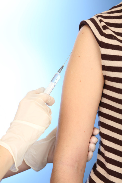 arts bedrijf spuit met een vaccin in de patiënt schouder, op blauwe achtergrond - Foto, afbeelding