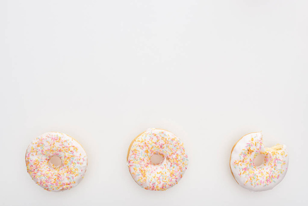 Top uitzicht van zoete hele donuts met hagelslag in de buurt van gebeten één op witte achtergrond - Foto, afbeelding