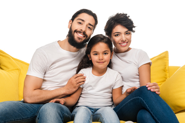 šťastní rodiče se usmívají, když sedí na pohovce s roztomilou dcerou izolovanou na bílém  - Fotografie, Obrázek