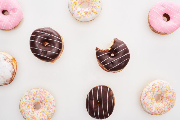 top view of colorful glazed delicious doughnuts and bitten one on white background - 写真・画像