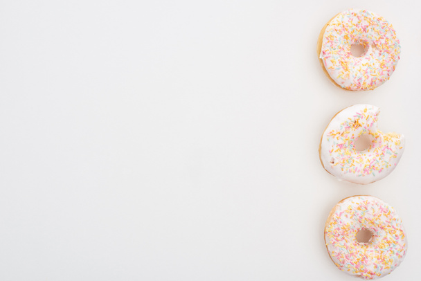 top view of whole doughnuts with sprinkles near bitten one on white background - Fotoğraf, Görsel