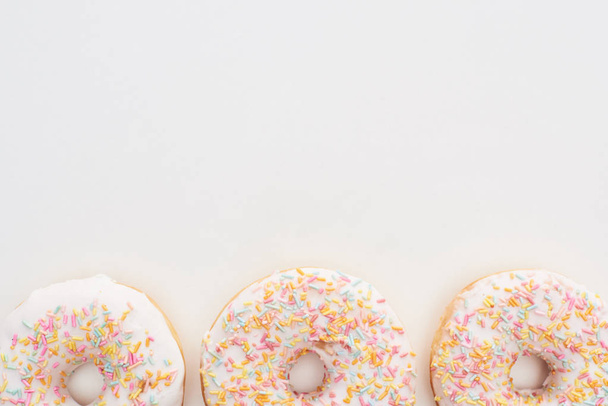 Top uitzicht van Wit geglazuurde donuts met hagelslag op witte achtergrond - Foto, afbeelding