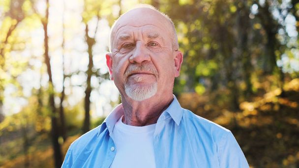 Active senior man walking in the park. Portrait of senior man with a beard smiling while standing outside in sunlight. - Foto, Imagen