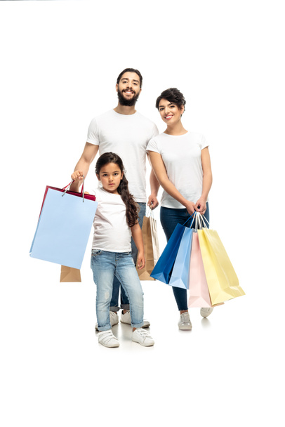 白で孤立したかわいい娘と一緒に立っている間、幸せなラテンの両親は買い物袋を持っています   - 写真・画像