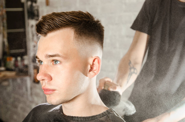 Barber cleans the neck of a young guy with a brush with talc after a haircut on a brick wall background - Foto, Bild