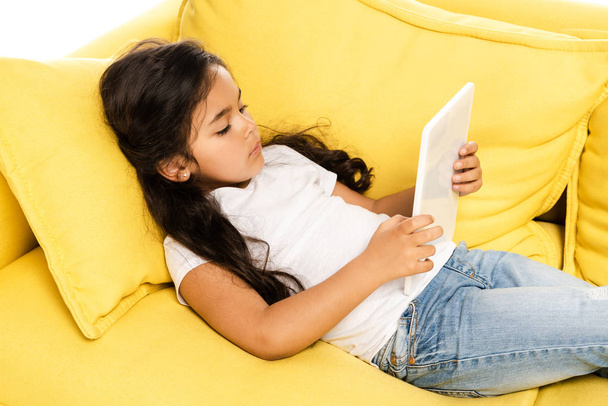 vue aérienne du mignon enfant latin couché sur un canapé jaune et utilisant une tablette numérique isolée sur blanc
  - Photo, image