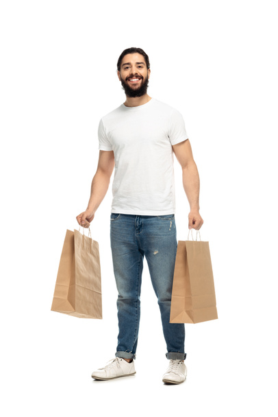 happy latin man holding shopping bags and smiling isolated on white  - Fotó, kép