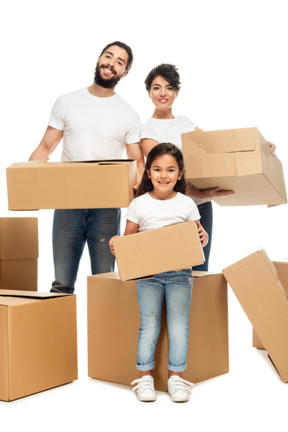 cheerful latin parents holding boxes and standing with cute daughter isolated on white  - Photo, Image