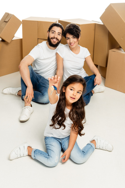 selective focus of cute latin kid holding keys and sitting near parents and boxes isolated on white  - Photo, Image