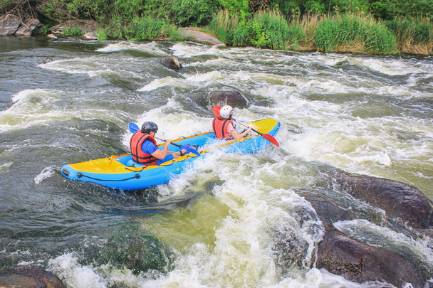 Νεαρό ζευγάρι απολαμβάνουν λευκό καγιάκ νερό στο ποτάμι, ακραία και διασκεδαστικό άθλημα στο τουριστικό αξιοθέατο. Ράφτινγκ στον ποταμό Πιβντένι Μπου. Ενεργό ζευγάρι περιπέτεια κατά μήκος του ποταμού - Φωτογραφία, εικόνα
