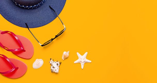 Аксессуары для летнего пляжа. Coral flip flops, blue straw hat, sunglasses, shells, starfish on yellow background view flat lay copy space. Летний фон. Концепция отпускного путешествия
. - Фото, изображение