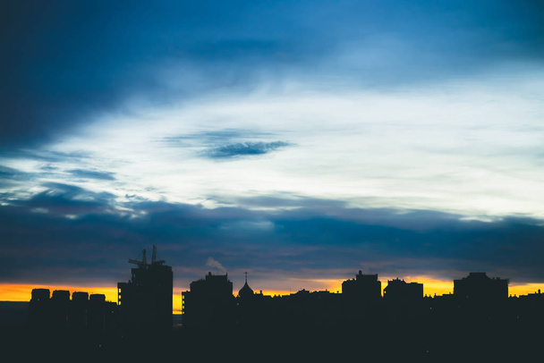 Αστικό τοπίο με υπέροχη ποικιλία έντονη αυγή. Εκπληκτική δραματική γαλάζια συννεφιά πάνω από τις σκοτεινές σιλουέτες των κτιρίων της πόλης. Ατμοσφαιρικό φόντο πορτοκαλί Ανατολή σε συννεφιασμένη καιρό. Αντιγραφή χώρου. - Φωτογραφία, εικόνα