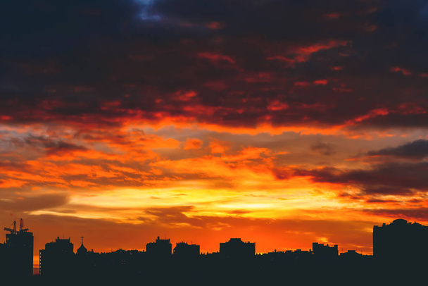 Cityscape with wonderful varicolored vivid fiery dawn. Amazing dramatic multicolored cloudy sky. Dark silhouettes of city buildings. Atmospheric background of sunrise in overcast weather. Copy space. - Photo, image