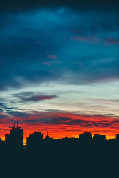 Αστικό τοπίο με υπέροχη ποικιλία έντονη αυγή. Εκπληκτικό δραματικό πολύχρωμο συννεφιασμένο ουρανό πάνω από σκοτεινές σιλουέτες των κτιρίων της πόλης. Ατμοσφαιρικό φόντο της αυγής σε συννεφιασμένη ατμόσφαιρα. Αντιγραφή χώρου. - Φωτογραφία, εικόνα