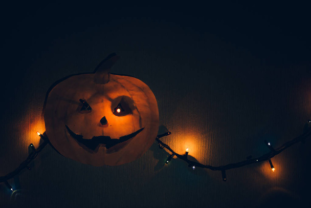 A paper pumpkin with a flashing garland in place of the eyes, hanging on the wall. A horrible template for Halloween. - Zdjęcie, obraz