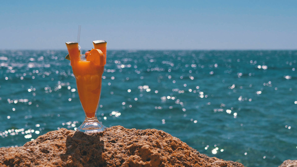 Tropical Fresh Cocktail w szklance ze słomy na plaży Egiptu stoi na skale na tle morza czerwonego - Materiał filmowy, wideo