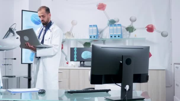 Dottore nel suo ufficio moderno in piedi e digitando al suo computer portatile
 - Filmati, video