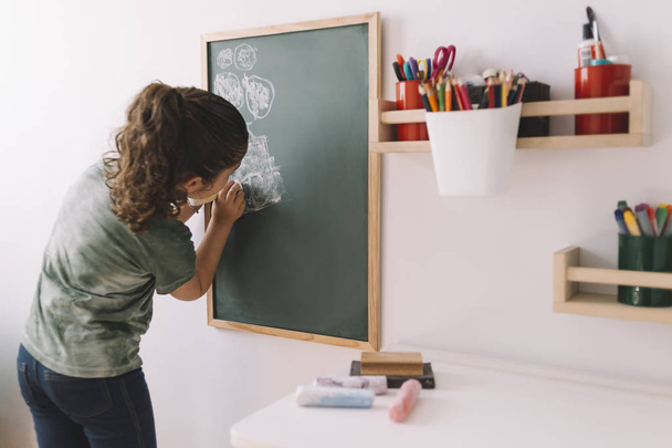 little girl drawing on a chalkboard at home - Фото, изображение