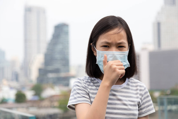 Petite fille asiatique souffrent de toux avec protection du masque facial, mignon enfant portant un masque facial en raison de la pollution de l'air dans le bâtiment de la ville comme fond, Fille malade avec masque médical ; concept de pollution, allergies à la poussière et la santé
 - Photo, image