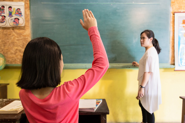 Profesora asiática enseñando a un niño en la escuela, niña sentada en el aula, estudiante levantando la mano para responder preguntas con libros en la mesa de estudio, educación, escuela primaria y concepto de aprendizaje
 - Foto, imagen
