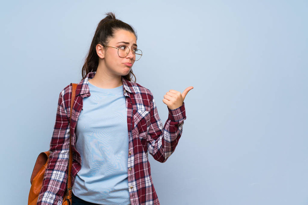 adolescente estudante menina sobre isolado azul parede infeliz e apontando para o lado
 - Foto, Imagem