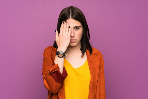 Giovane donna in un cappotto su sfondo viola isolato che copre un occhio a mano
 - Foto, immagini