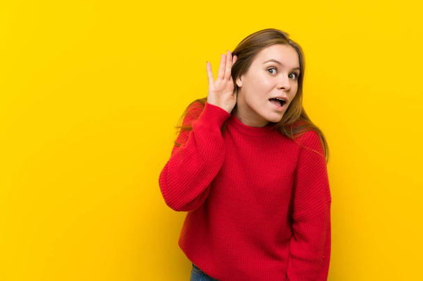 junge Frau über gelbe Wand hört etwas, indem sie die Hand ans Ohr legt - Foto, Bild