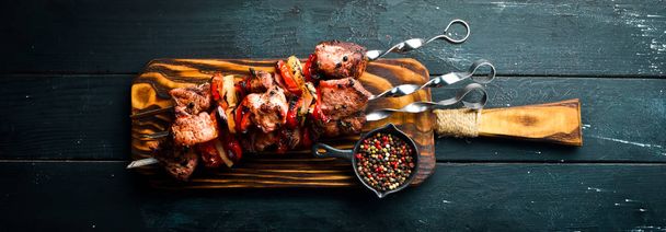 Shish kebab BBQ meat with onions and tomatoes. On a black background. Top view. Free space for your text. Rustic style. - Foto, Imagem