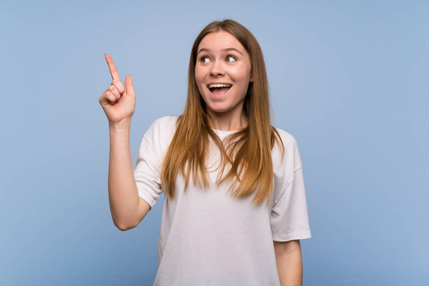 Young woman over blue wall intending to realizes the solution while lifting a finger up - Photo, Image