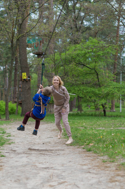 Mama rolkach syna na stacji kolejki linowej. Zajęcia rekreacyjne w parku. Wzajemne oddziaływanie między matką a dzieckiem. - Zdjęcie, obraz