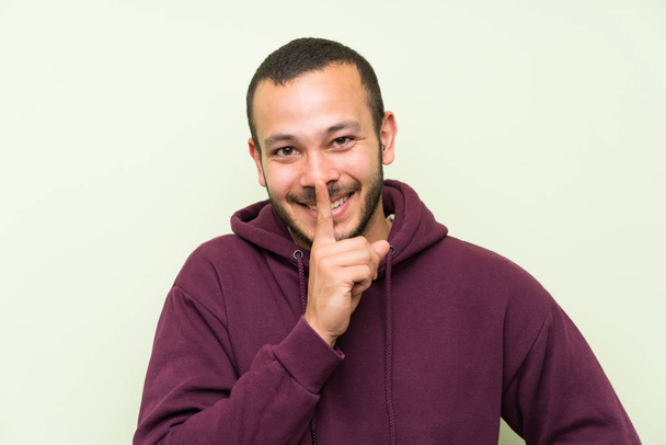 Colombian man with sweatshirt over green wall doing silence gesture - Foto, Imagen