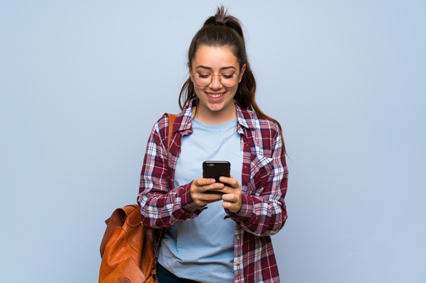 Девочка-подросток через изолированную голубую стену отправляет сообщение с мобильным телефоном
 - Фото, изображение