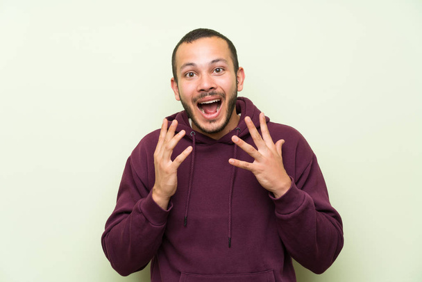 Homem colombiano com camisola sobre parede verde com expressão facial surpresa
 - Foto, Imagem