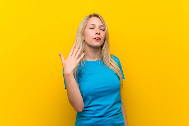 Jonge blonde vrouw over geïsoleerde gele achtergrond met vermoeide en zieke uitdrukking - Foto, afbeelding
