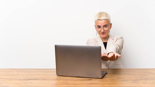 Menina adolescente com cabelo curto com um laptop segurando copyspace imaginário na palma da mão para inserir um anúncio
 - Foto, Imagem