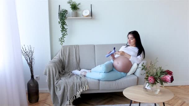 Νεαρή έγκυος γυναίκα μέσα. έγκυος γυναίκα που βάζει κρέμα  - Πλάνα, βίντεο