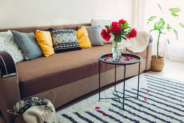 Innenraum des Wohnzimmers mit Blumen, Pflanzen und Teppich dekoriert. Gemütliche Couch mit Kissen und Tisch - Foto, Bild