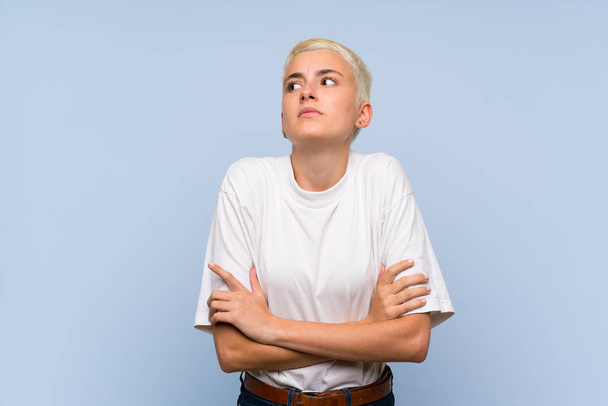 Adolescente chica con el pelo corto blanco sobre la pared azul haciendo gesto dudas mientras levanta los hombros
 - Foto, imagen