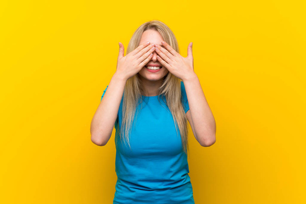 Giovane donna bionda su sfondo giallo isolato che copre gli occhi dalle mani
 - Foto, immagini