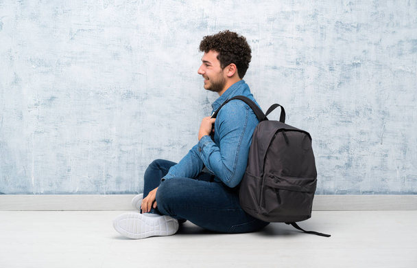 Молодой человек сидит на полу с рюкзаком
 - Фото, изображение