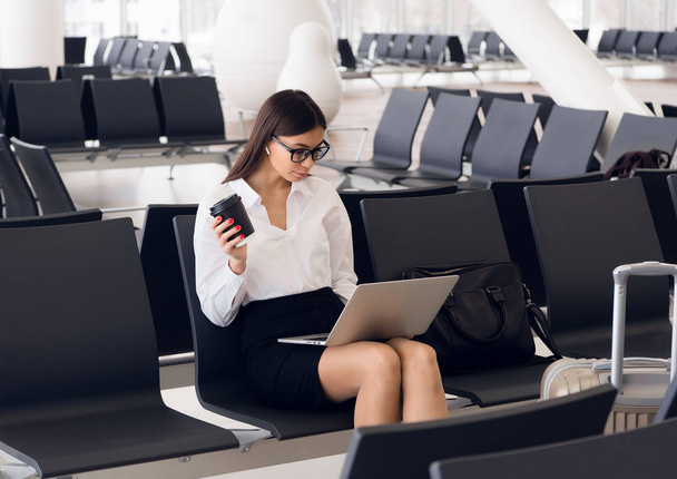 Випадкова жінка працює на ноутбуці в залі аеропорту. Жінка чекає свого польоту в терміналі аеропорту, сидить на стільці і друкує на ноутбуці
 - Фото, зображення